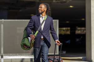 Man carrying his pet's rolled up RuffRest slung across his shoulder, while towing his carry on luggage at the airport, dog beds for large dogs, dog bed for small dogs