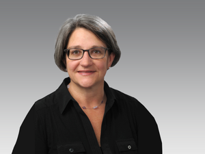Professional headshot or image of a woman with silver and black hair, in a black blouse, wearing glasses and a necklace. She is an attorney who has helped Timberdog, a dog bed company, acquire two trademarks
